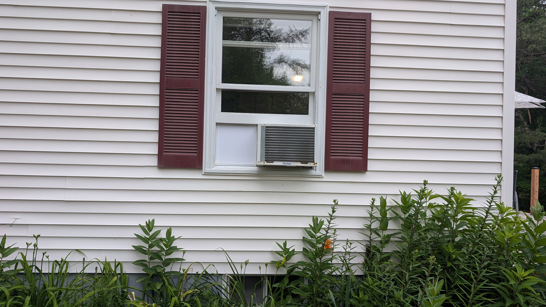 Window air conditioner unit on a house exterior with greenery around using Easy AC Screen